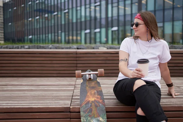 Yaz günü kaykay yakınında ahşap bankta oturan elinde cam ile spor esmer kadın Portresi