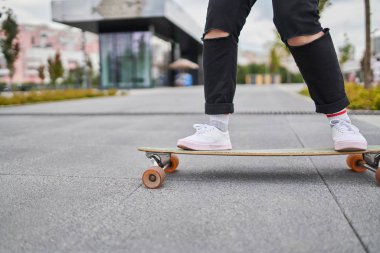 Image of legs of woman in black jeans riding skateboard on street in city clipart