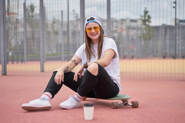 Imagem de menina morena atlética sorridente em óculos de sol sentados no skate no playground no dia de verão — Fotografia de Stock