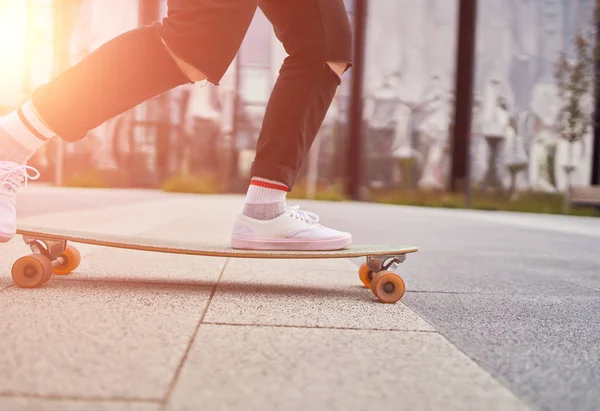 Picture of womans legs in white sneakers riding skateboard on street in city on summer day.