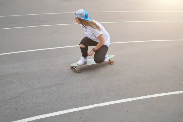 Photo on side of young brunette girl in baseball cap riding skateboard outdoors — Stock Photo, Image