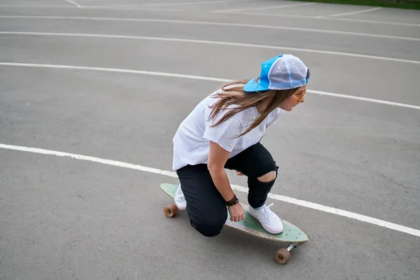 Foto auf der Seite einer jungen brünetten Frau mit Baseballmütze, die im Freien Skateboard fährt — Stockfoto