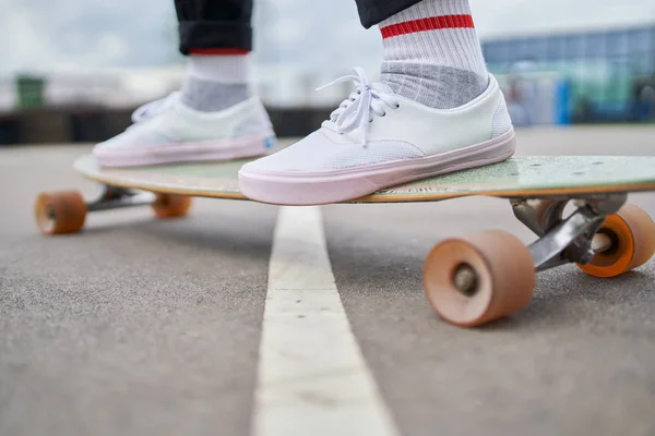 Photo of womans legs in white sneakers riding skateboard on street in city