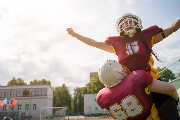 Bild zweier amerikanischer Football-Sportlerinnen, die Helme mit den Händen zur Seite gegen den bewölkten Himmel tragen — Stockfoto