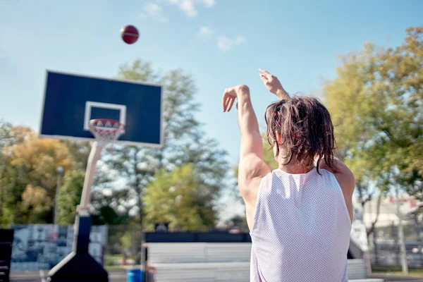 Foto van rug van atleet gooien bal in basketbal hoepel tegen blauwe hemel — Stockfoto