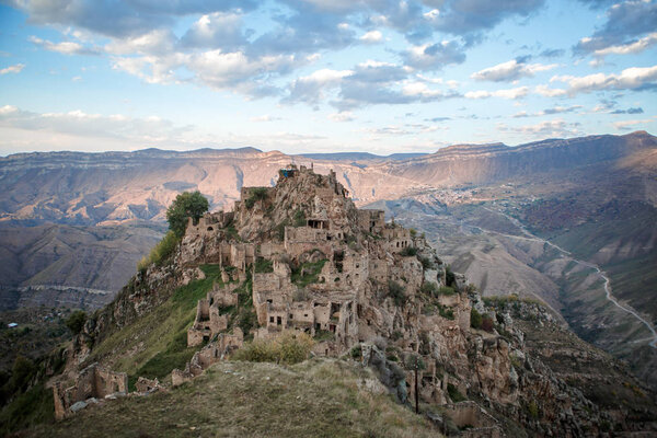 Изображение древних руин, горной местности с зеленой растительностью на фоне облачно-голубого неба
