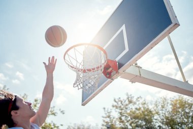 Mavi gökyüzüne karşı basketbol potasına top atan atletfotoğrafı