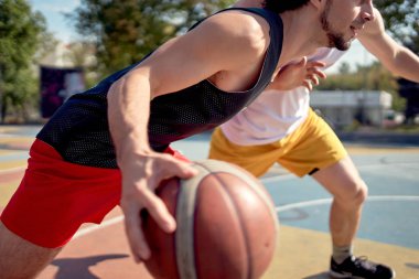 Yaz gününde oyun alanında basketbol oynayan genç sporcuların görüntüsü.