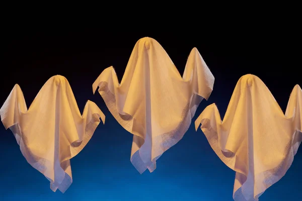 Imagen de tres fantasmas de Halloween hechos de tela blanca sobre fondo negro y azul . —  Fotos de Stock