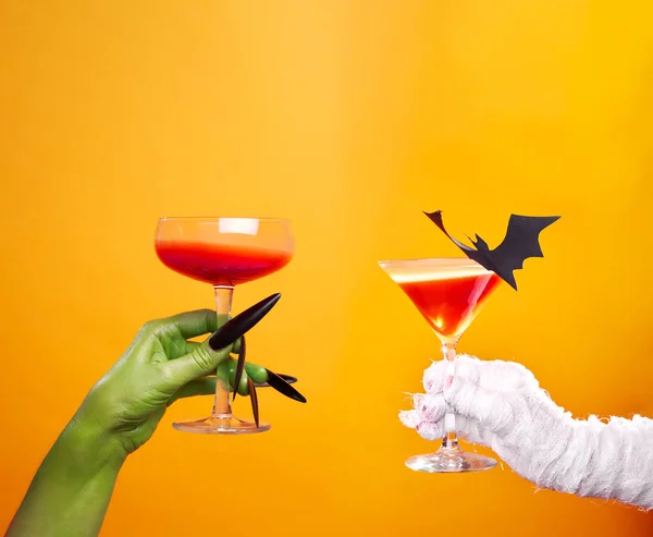 Foto der Hände von Mumie und Zombies mit Weinglas und schwarzer Fledermaus auf leerem orangefarbenem Hintergrund . — Stockfoto