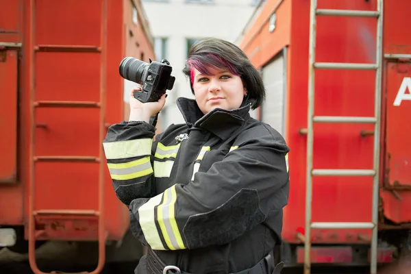 Bild av Brunette brandman med kamera till hands står bredvid brandmän bil. — Stockfoto