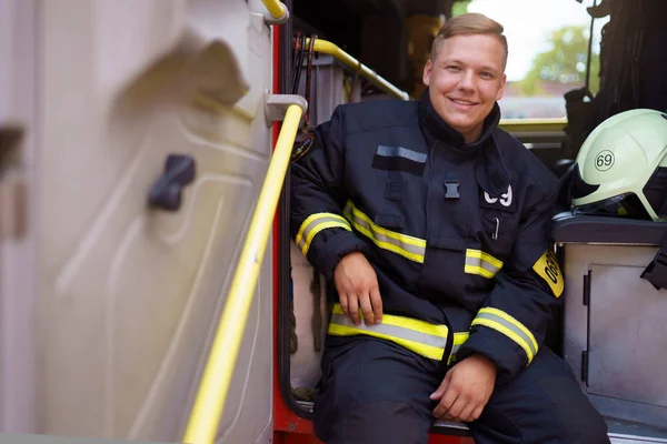 Foto de bombero sonriente sentado en camión de bomberos en la estación de bomberos — Foto de Stock