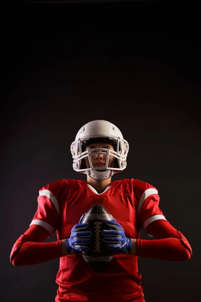 Foto de una futbolista americana en casco con pelota de rugby en las manos sobre fondo negro en blanco —  Fotos de Stock