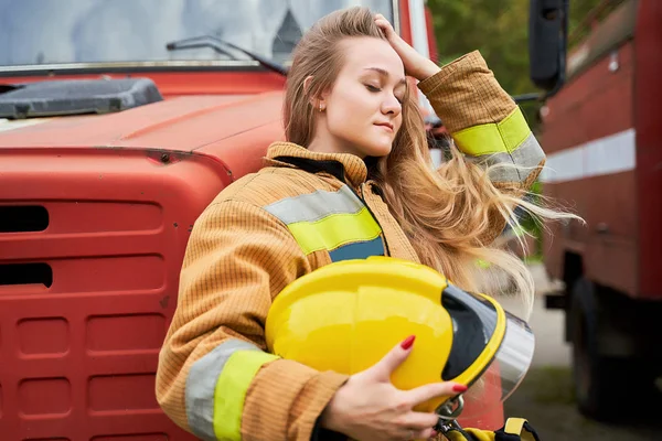 Foto de jovem bombeiro loiro no fundo dos motores de incêndio — Fotografia de Stock