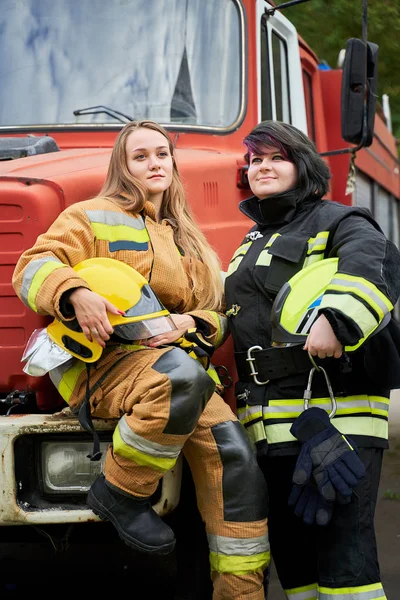 Volledige foto van twee jonge brandweerlieden op de achtergrond van brandweerauto 's — Stockfoto