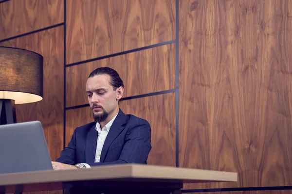 Foto des jungen Geschäftsmannes am Tisch sitzend mit Laptop auf dem Hintergrund der Holzwand. — Stockfoto