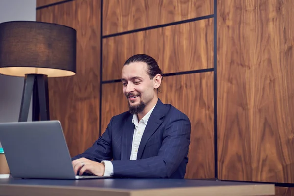 Immagine di uomo d'affari felice seduto a tavola con computer portatile sullo sfondo della parete di legno . — Foto Stock