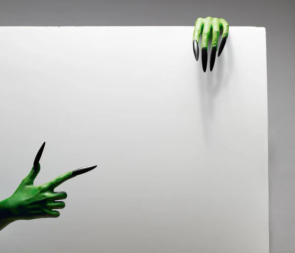 Concepto de Halloween. Dos manos verdes sostienen hoja de papel gris en blanco en el estudio . — Foto de Stock