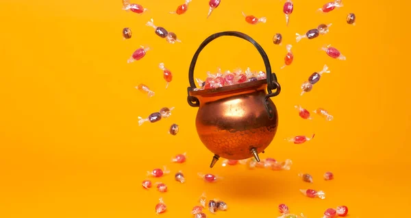 Dzbanek żelazny z wielobarwnymi karmelami na pustym pomarańczowym tle. — Zdjęcie stockowe