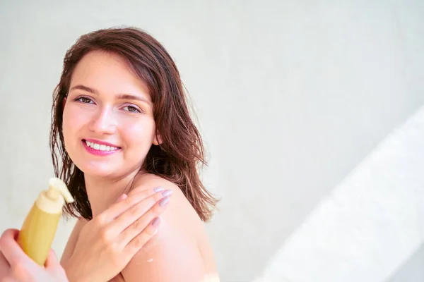 Foto da menina feliz com loção corporal em suas mãos sobre fundo cinza em branco . — Fotografia de Stock