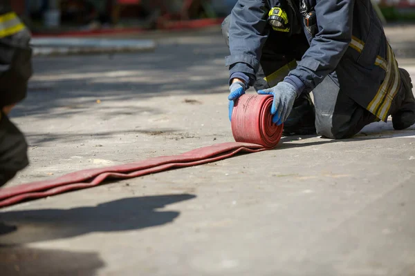 Feuerwehrmann wickelt roten Feuerwehrschlauch im Freien ab — Stockfoto