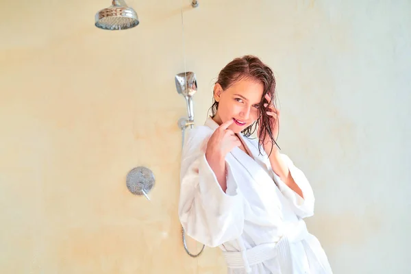 Foto di felice donna bruna con i capelli bagnati in accappatoio bianco in piedi in bagno . — Foto Stock