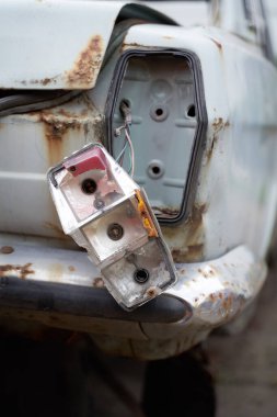 Kırık farları olan paslı beyaz bir araba.