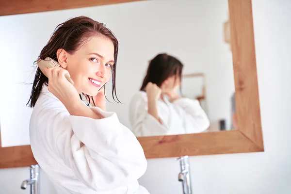 Zdjęcie brunetki czesającej włosy przed lustrem w łazience . — Zdjęcie stockowe