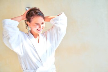 Beyaz bornozlu, sırılsıklam saçlı esmer bir kızın banyo yaparken çekilmiş fotoğrafı..