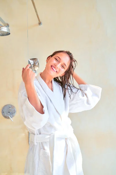 Foto de mujer morena feliz con el pelo mojado en albornoz blanco de pie en el baño . — Foto de Stock