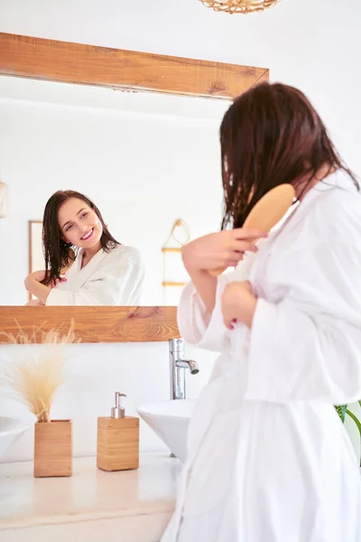 Obraz brunetki czesającej włosy przed lustrem w łazience — Zdjęcie stockowe