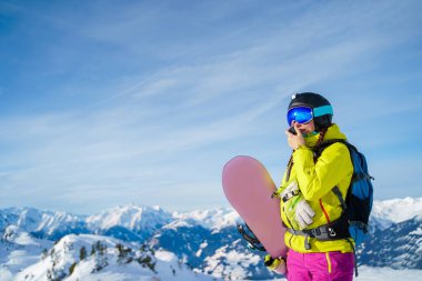 Kasklı ve maskeli, kar yamacında duran walkie-talkie ve snowboard 'lu atletik kadın..