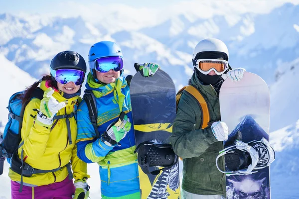 Foto van drie blije snowboarders in helm op achtergrond bergen. — Stockfoto