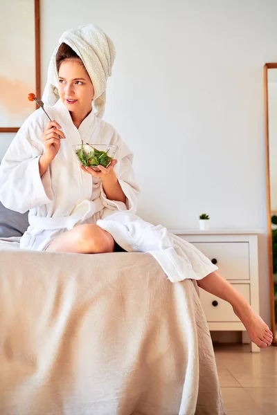 Zdjęcie kobiety w szlafroku z sałatką na łóżku. — Zdjęcie stockowe