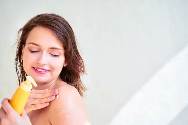 Foto di giovane ragazza con lozione corpo nelle sue mani su sfondo grigio bianco — Foto Stock