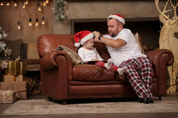 Foto de padre en Santa hat e hijo en sofá rojo en la habitación —  Fotos de Stock