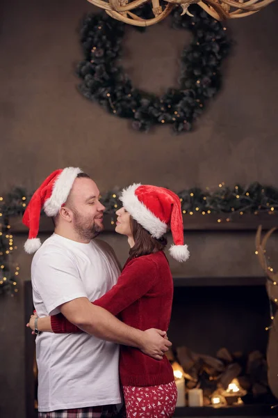 Foto di abbracciare uomini e donne a Babbo Natale cappello in camera — Foto Stock