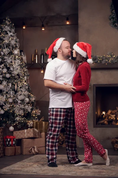 Foto lateral de abrazar a hombres y mujeres en gorra de Santas en la habitación — Foto de Stock