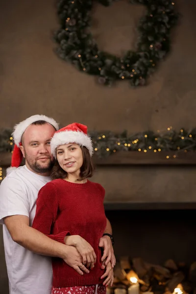 Ritratto di abbracciare uomini e donne in berretto e pigiama di Babbo Natale in camera — Foto Stock