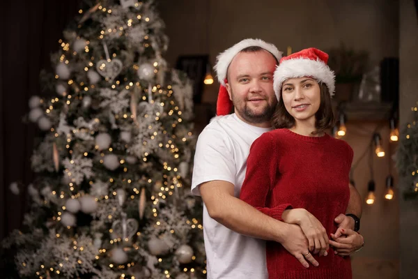 Image of embracing men and women in Santas cap on background of Christmas tree in room — Stock Photo, Image