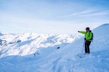 Karlı yamaçta kayak yaparken elini gösteren atletik bir adam.