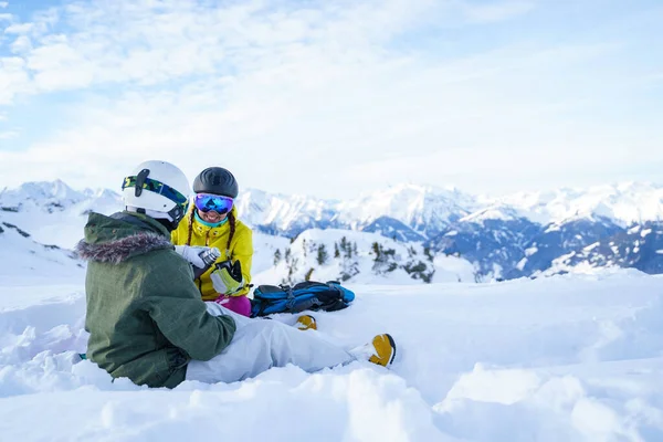 Zdjęcie dwóch sportowców z termosem w rękach siedzących na śnieżnym kurorcie. — Zdjęcie stockowe