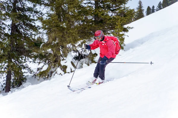 Imagen lateral del deportista en chaqueta roja y con mochila esquiando en estación de invierno —  Fotos de Stock