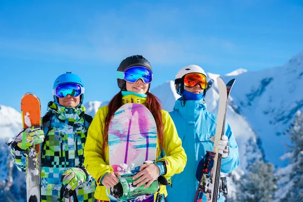 Homem e mulher felizes com snowboard e esquis em pé no resort de neve contra o pano de fundo da montanha à tarde . — Fotografia de Stock