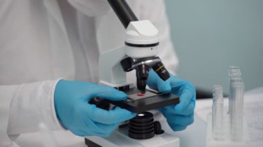 Kadın bilim adamı bazı test materyalleri yerleştirir ve bir laboratuarda mikroskoba bakar..