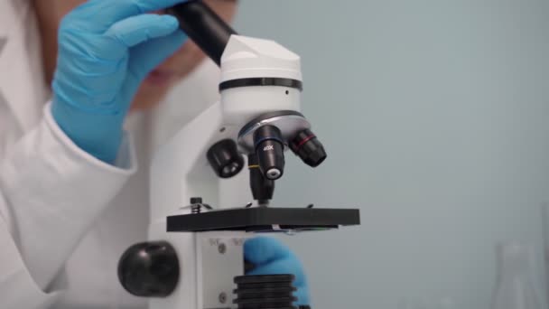 Vrouwelijke medisch onderzoeker die door de microscoop kijkt. — Stockvideo