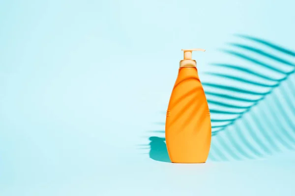 Recipiente laranja para loção sem etiqueta em fundo azul com folha — Fotografia de Stock