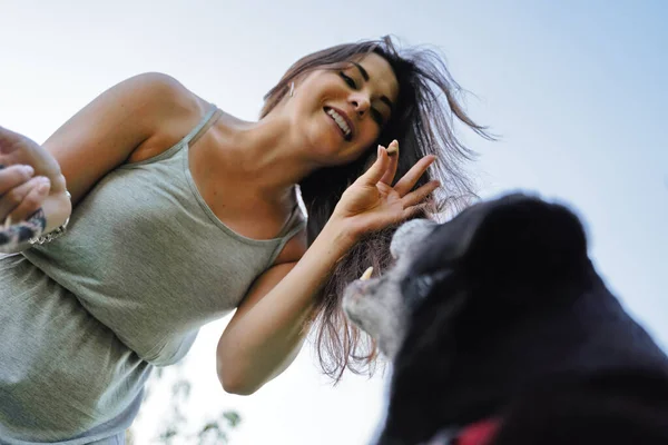Szczęśliwa kobieta i czarny pies przeciwko błękitnemu niebu po południu — Zdjęcie stockowe