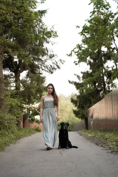 Mulher morena no passeio com cão preto no parque no verão — Fotografia de Stock