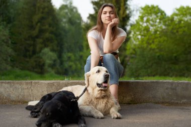 Pensive woman squatting next to dog on summer day. clipart